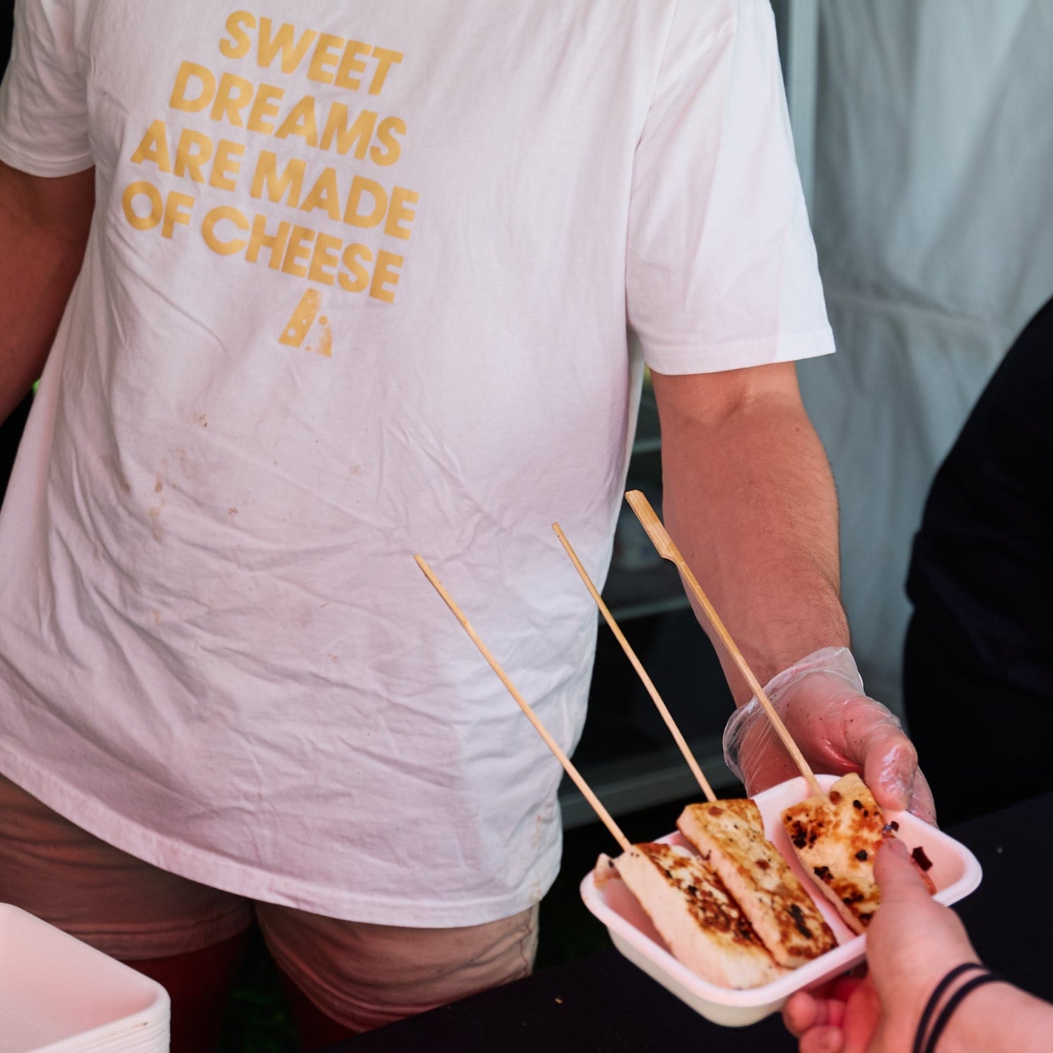 Man in a white t-shirt with yellow text standing behind a counter, serving food.